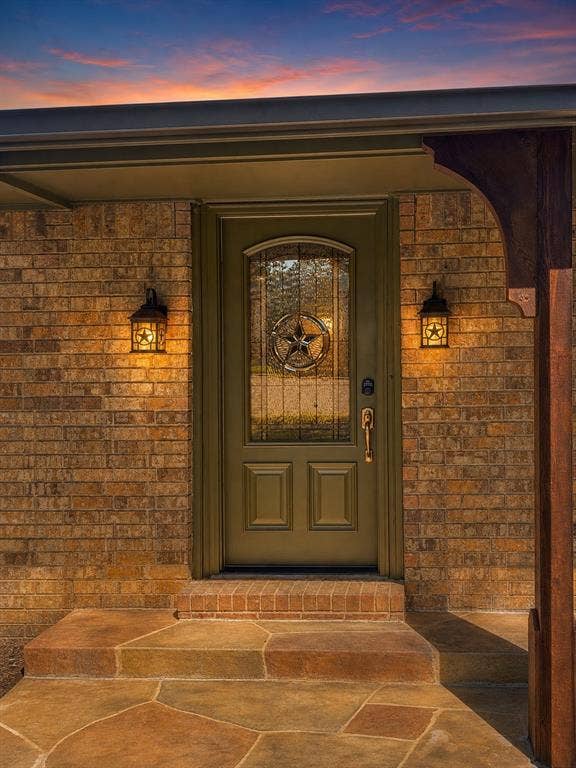 3210 Cortez Court W, Irving, TX 75062 Brick exterior entry featuring a flagstone porch, arched wood-finish front door with decorative glass inlay, and two wall-mounted metal light fixtures