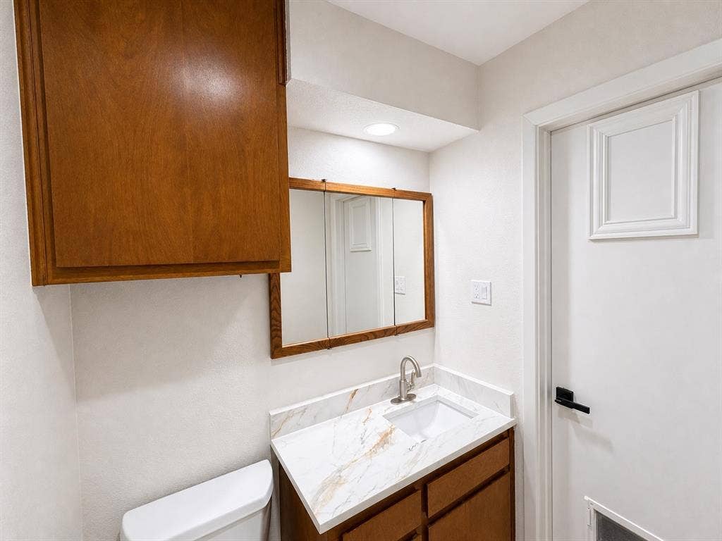 3210 Cortez Court W, Irving, TX 75062 Bathroom featuring a vanity with a stone-finish countertop, undermount sink, brushed nickel faucet, wall-mounted wood-finish cabinetry, and a tri-fold medicine cabinet