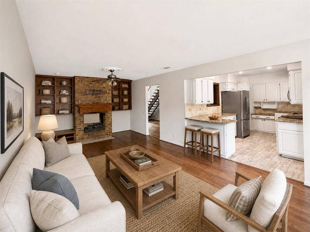 3210 Cortez Court W, Irving, TX 75062 Living area featuring a floor-to-ceiling brick fireplace with wood-finish built-in shelving, wood-finish flooring, and kitchen with white cabinetry and stone countertops