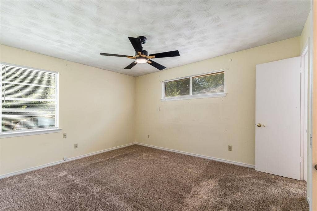 Room featuring neutral wall tones, carpeted flooring, a ceiling fan with integrated lighting, dual windows, and a solid interior door