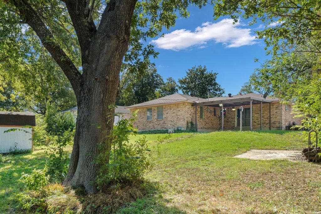 Brick exterior, covered patio, and mature trees situated on a spacious lot