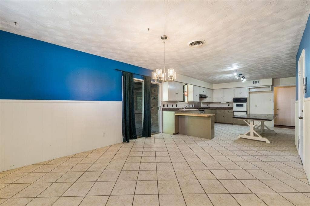Open-concept interior featuring light-colored ceramic tile flooring, a peninsula island, built-in wall oven, and a multi-light chandelier