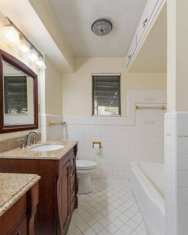 Dark wood vanity with stone countertop, drop-in sink, wall-mounted mirror, white ceramic tile wainscoting, and built-in upper storage cabinetry