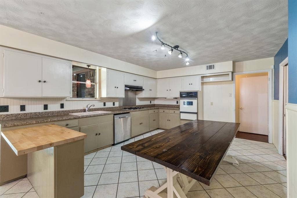 Kitchen featuring white upper cabinetry, multi-toned lower cabinetry, stainless steel dishwasher, built-in wall oven, and ceramic tile flooring