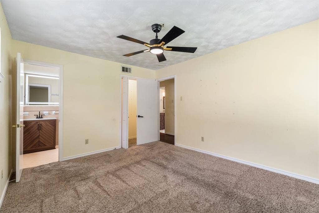 Interior room featuring neutral carpeting, a central ceiling fan with integrated lighting, and multiple points of entry