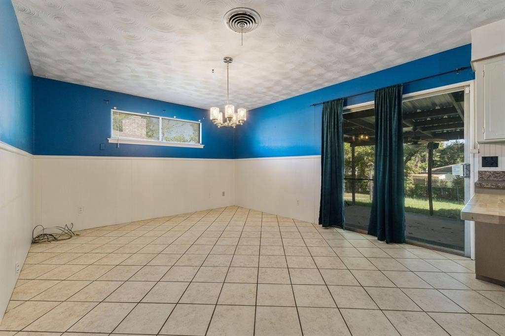 Spacious room featuring tile flooring, horizontal wall paneling, a multi-light chandelier, and glass sliding doors providing exterior access