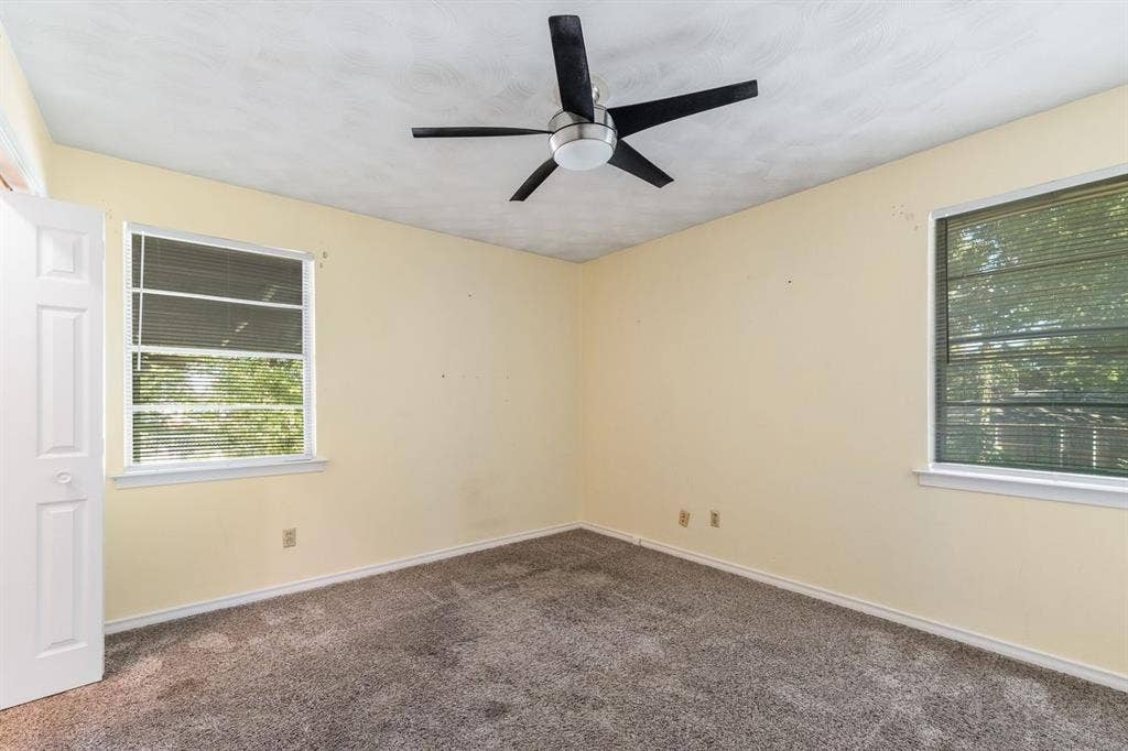 Interior room featuring neutral wall paint, wall-to-wall carpeting, two dual-pane windows, and a ceiling-mounted fan with integrated lighting