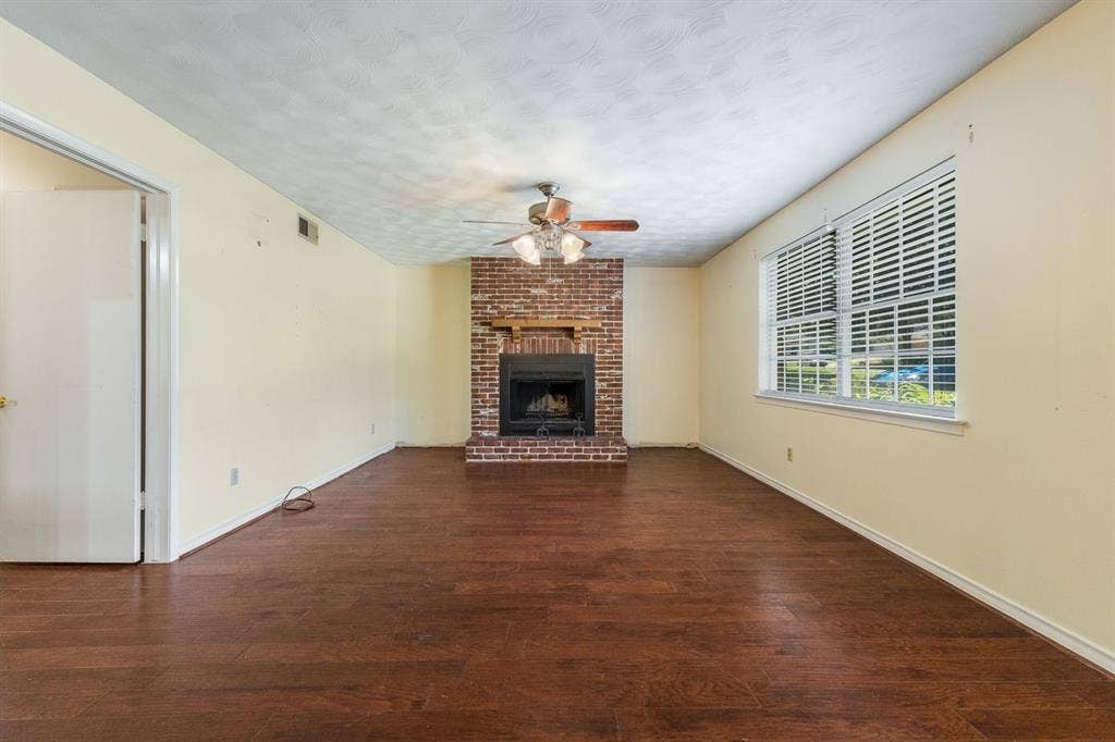 Exposed brick fireplace with a wood mantel, wood-finish flooring, and a ceiling-mounted light fixture with fan blades
