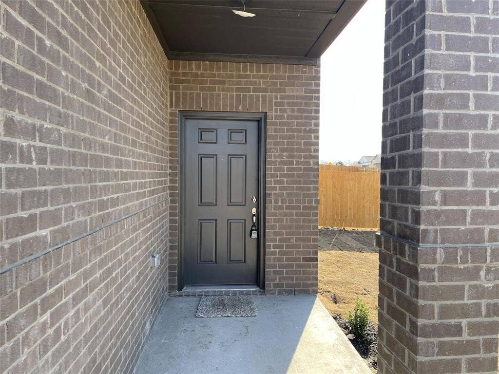 Covered entryway featuring dark brick masonry, a solid six-panel door, and a concrete porch foundation