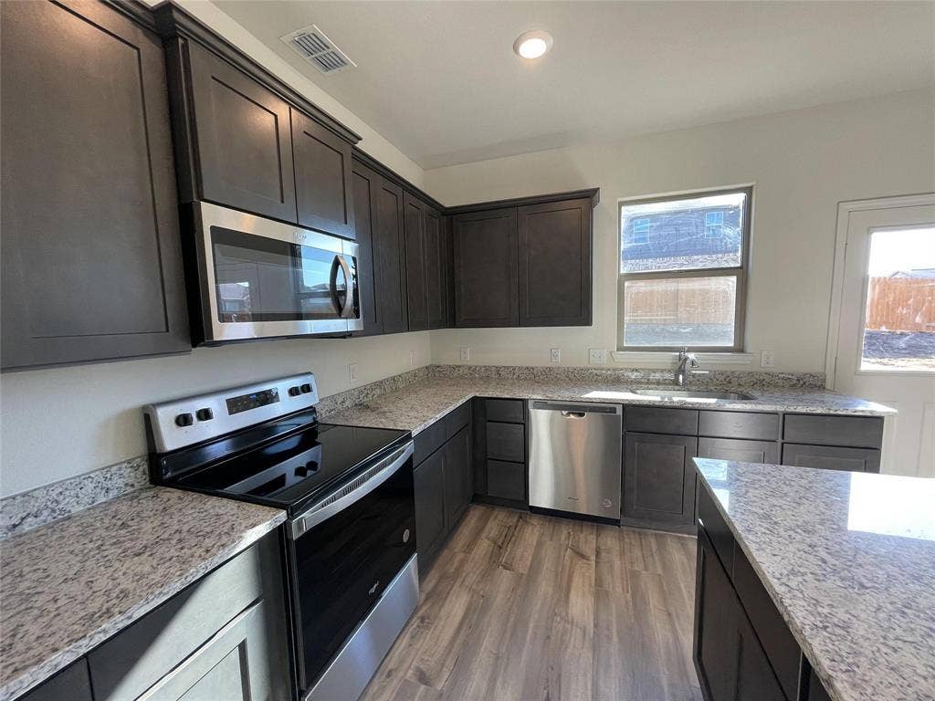 Kitchen featuring dark cabinetry, stone-finish countertops, stainless steel appliances, and wood-finish flooring
