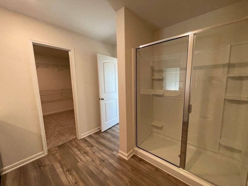 Bathroom featuring a glass-enclosed shower stall with integrated shelving, wood-finish flooring, and a walk-in closet with wire shelving