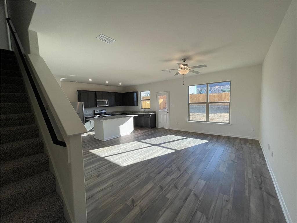 Open floor plan featuring wood-finish flooring, a kitchen island, dark cabinetry, and a ceiling fan