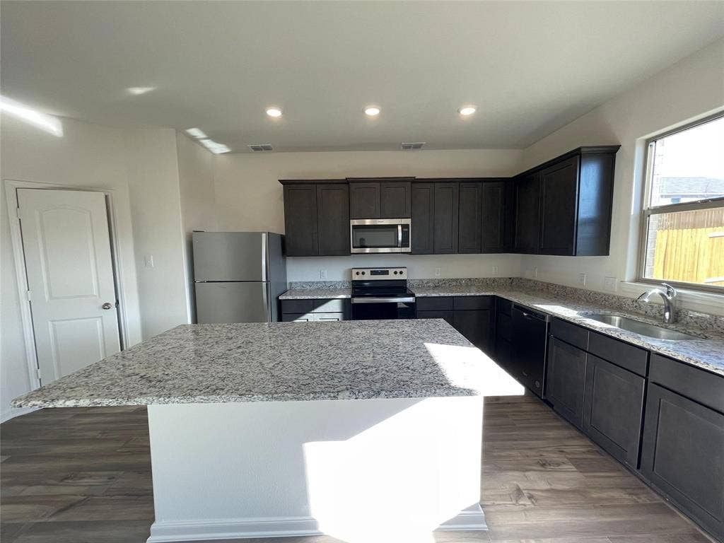 Kitchen featuring dark cabinetry, stone-surface countertops, center island, stainless steel appliances, and wood-finish flooring