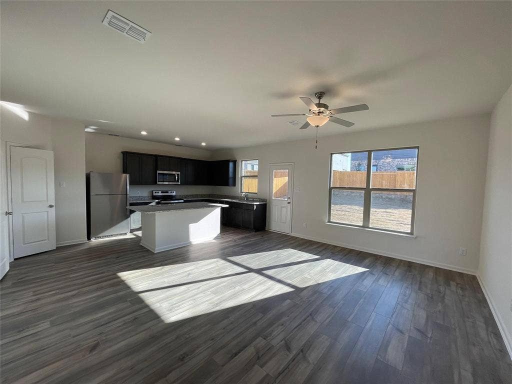 Open-concept kitchen featuring dark cabinetry, a central island, stainless steel appliances, wood-finish flooring, and a ceiling fan