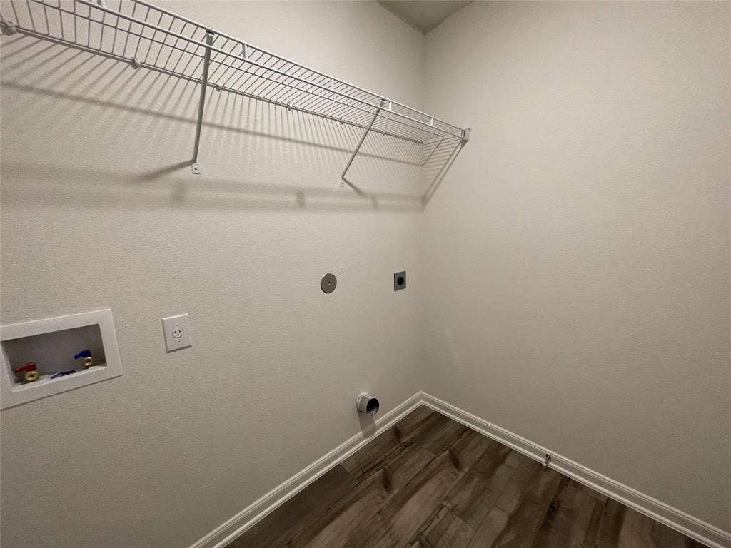 Utility space featuring wood-finish flooring, a wall-mounted wire shelving system, and dedicated water and electrical hookups