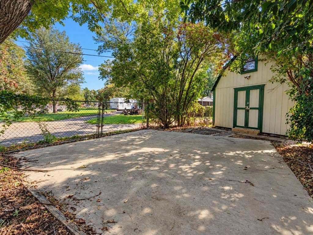 Concrete patio area featuring a detached outbuilding with vertical siding, double-door entry, and chain-link perimeter fencing