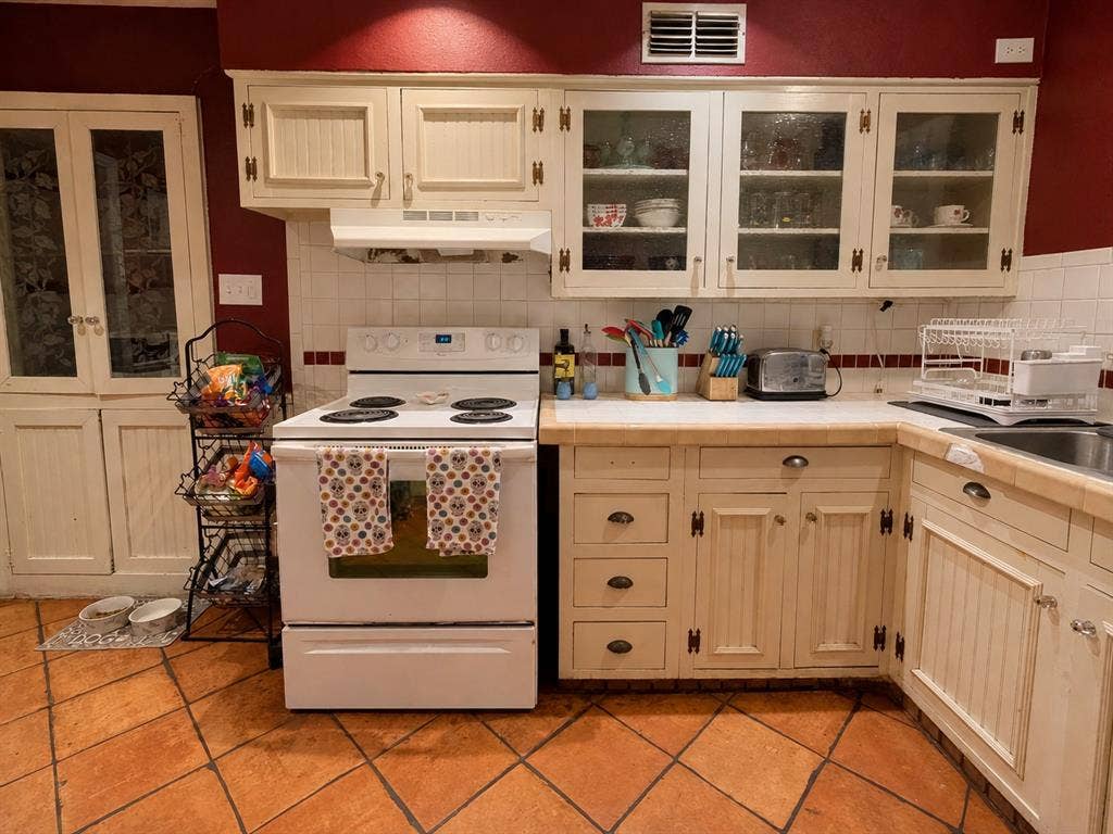 Kitchen featuring off-white cabinetry with glass-front display uppers, tile countertops, terracotta flooring, a built-in pantry, and a white electric range