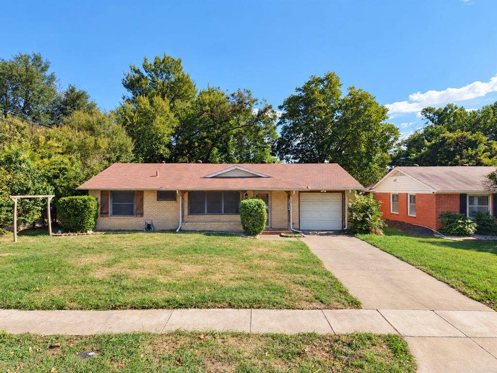 Single-story brick exterior featuring a shingled roof, attached one-car garage, concrete driveway, and front lawn