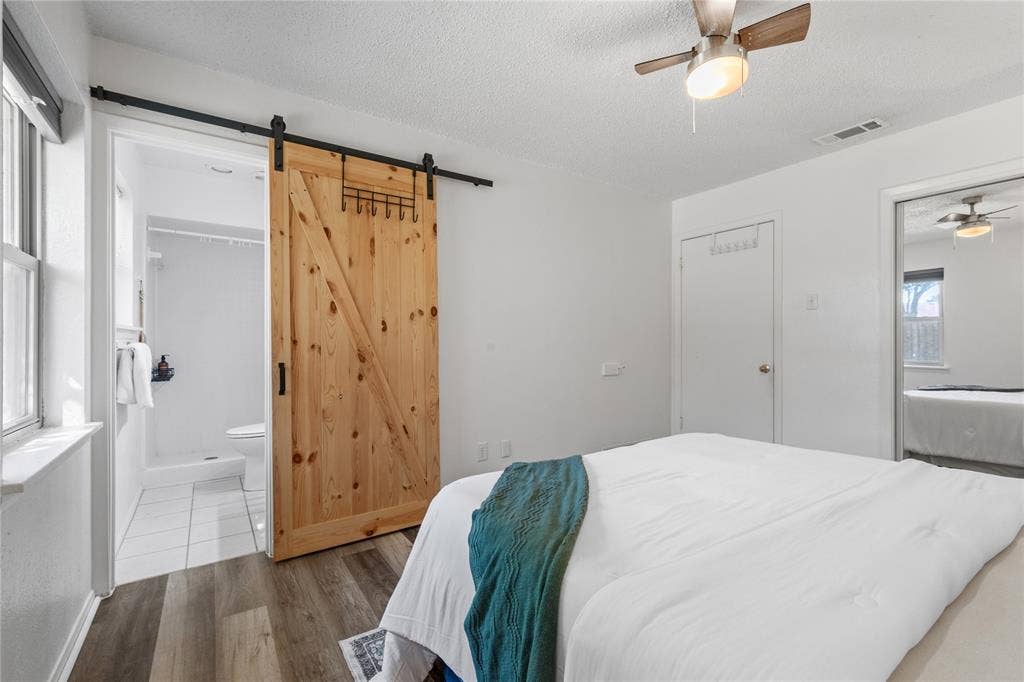 907 Crest Park Drive, Garland, TX 75042 Bedroom featuring wood-finish flooring, a wood-panel barn door with matte black hardware, and a ceiling fan with integrated light fixture