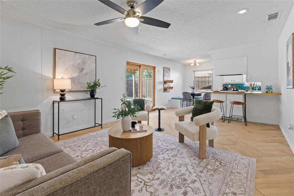 907 Crest Park Drive, Garland, TX 75042 Open-concept interior featuring light wood-finish herringbone flooring, a built-in kitchen breakfast bar, a modern ceiling fan, and sliding glass doors with exterior access