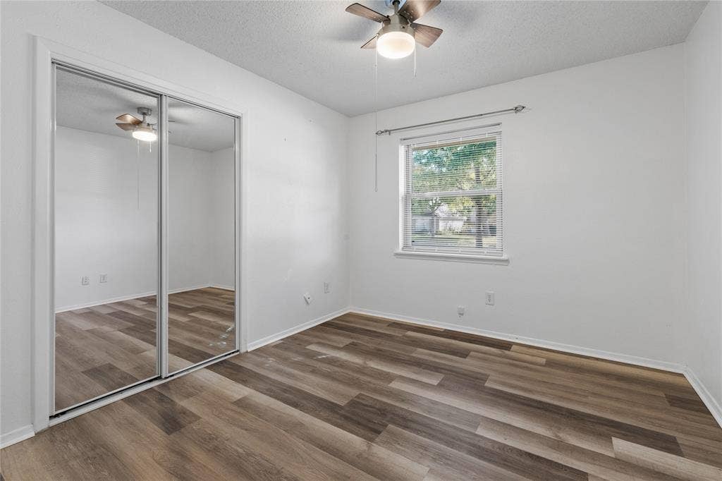 907 Crest Park Drive, Garland, TX 75042 Room featuring wood-finish flooring, sliding mirrored closet doors, a single-hung window, and a ceiling fan with integrated light fixture