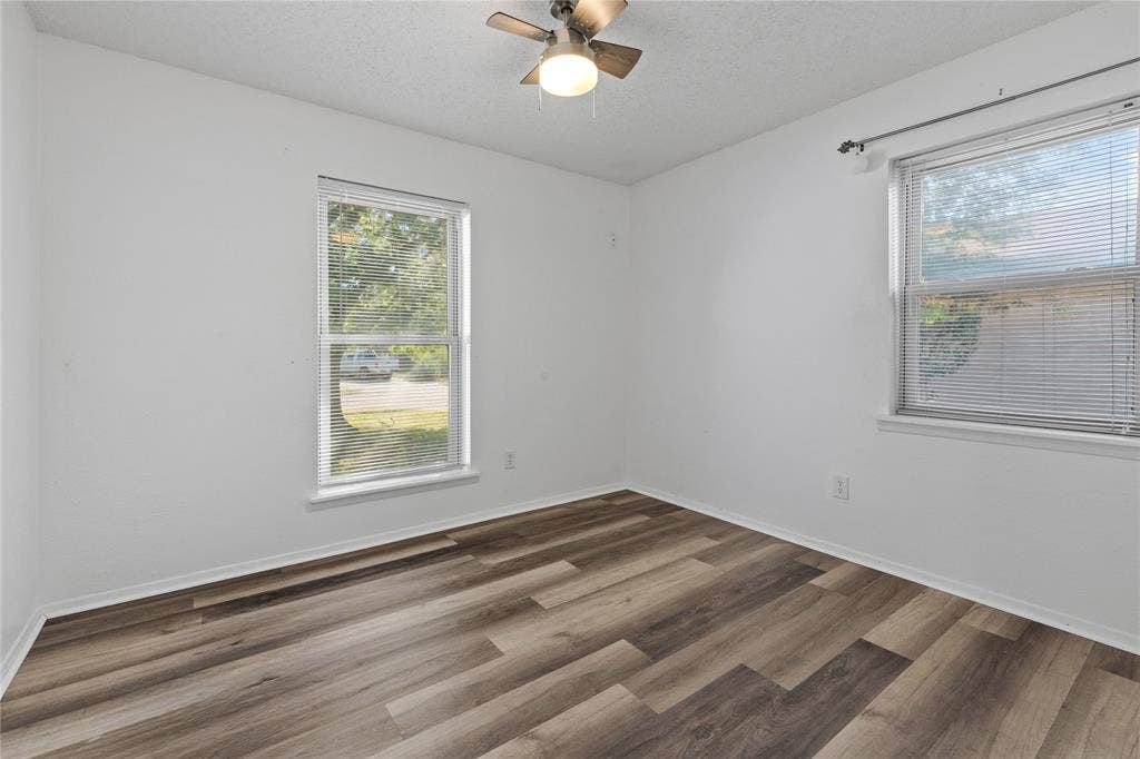 907 Crest Park Drive, Garland, TX 75042 Room featuring wood-finish flooring, two windows with horizontal blinds, and a ceiling-mounted light fixture with fan blades
