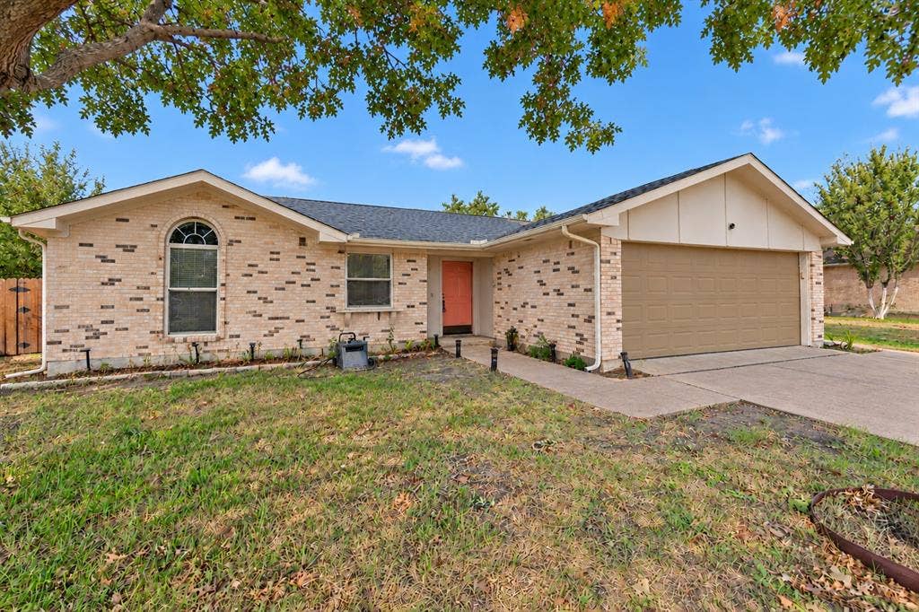 907 Crest Park Drive, Garland, TX 75042 Single-story brick exterior featuring an arched window, asphalt shingle roof, concrete driveway, and attached two-car garage
