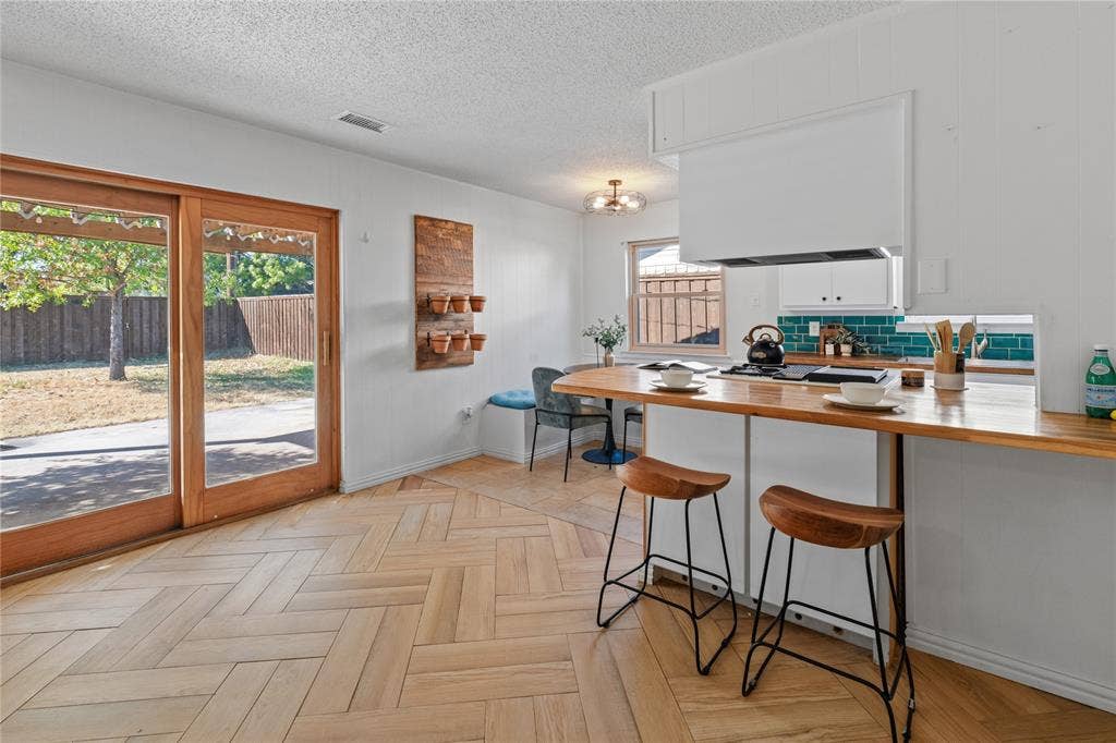 907 Crest Park Drive, Garland, TX 75042 Herringbone-pattern wood-finish flooring, breakfast bar with wood countertop, teal tile backsplash, and wooden-frame sliding glass door