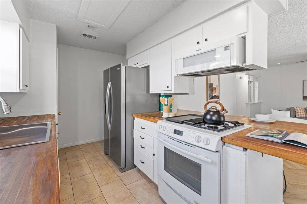 907 Crest Park Drive, Garland, TX 75042 Kitchen featuring white cabinetry, wood-finish countertops, tile flooring, and stainless steel appliances