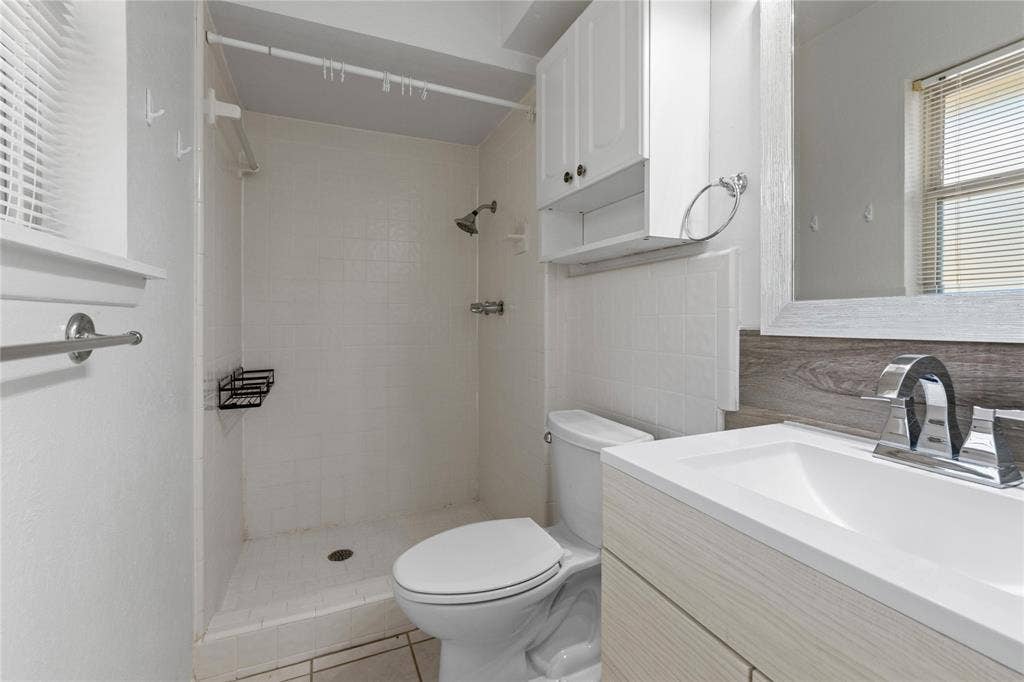 907 Crest Park Drive, Garland, TX 75042 Bathroom featuring a wood-finish vanity with a rectangular sink, chrome fixtures, tiled shower enclosure, and built-in upper cabinetry