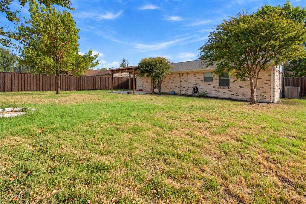 907 Crest Park Drive, Garland, TX 75042 Brick exterior finish, wooden pergola, and expansive fenced yard with mature trees