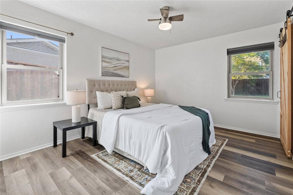 907 Crest Park Drive, Garland, TX 75042 Bedroom with wood-finish flooring, dual windows with roller shades, a ceiling fan with integrated lighting, and a sliding barn-style door