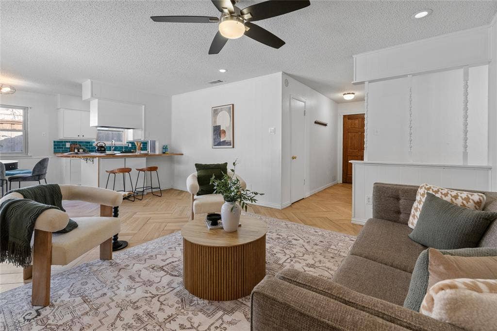 907 Crest Park Drive, Garland, TX 75042 Open-concept space featuring herringbone-pattern wood-finish flooring, a kitchen breakfast bar with integrated cabinetry, ceiling-mounted paddle fan, and recessed lighting