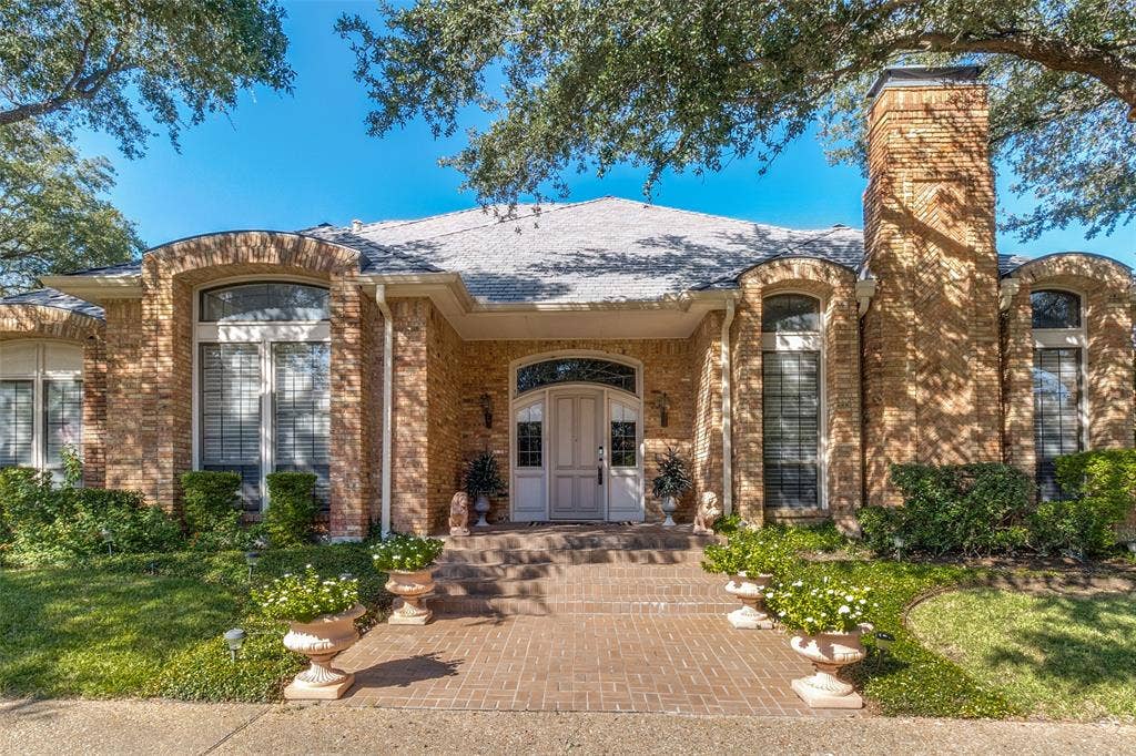 6215 Raintree Court, Dallas, TX 75254 Brick exterior featuring an arched entryway, detailed masonry work, a covered front porch, and tall windows with transoms