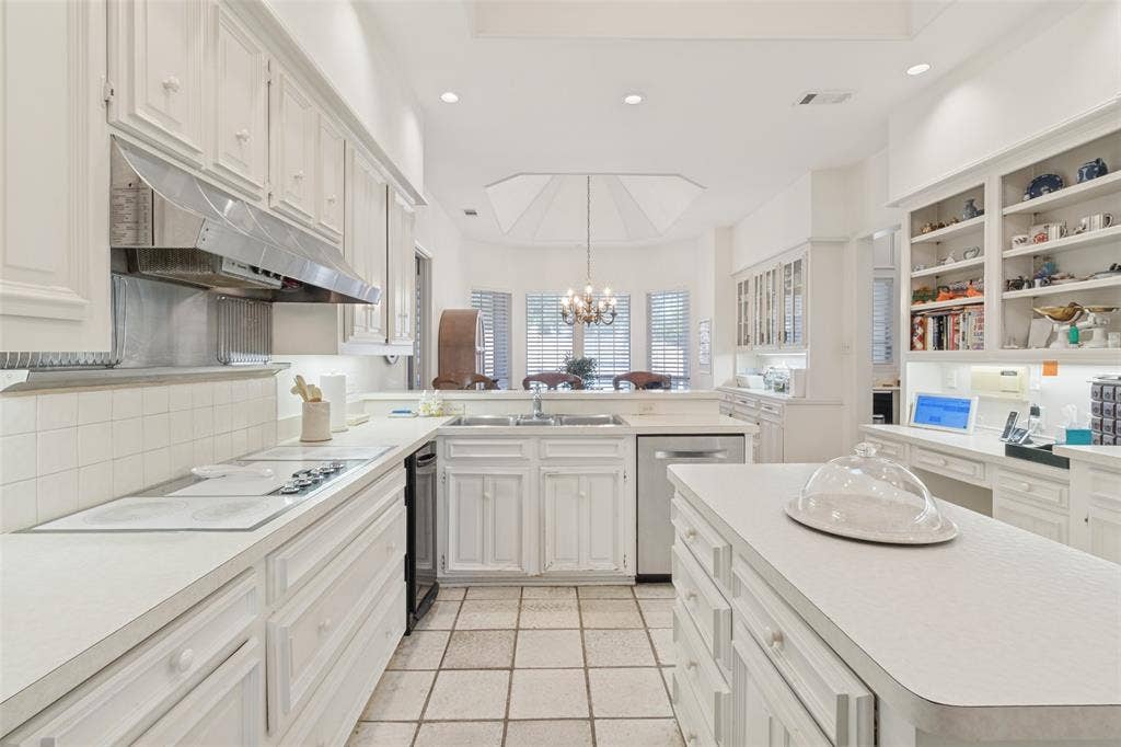 6215 Raintree Court, Dallas, TX 75254 Kitchen featuring white cabinetry, center island, stainless steel range hood, built-in shelving, and tile flooring