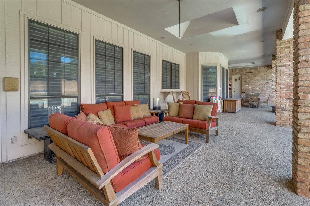 6215 Raintree Court, Dallas, TX 75254 Covered patio featuring aggregate concrete flooring, recessed lighting, brick column accents, and vertical exterior siding