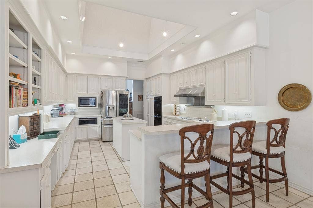 6215 Raintree Court, Dallas, TX 75254 Kitchen featuring white cabinetry, central island with prep sink, recessed ceiling lighting, tile flooring, and integrated stainless steel appliances