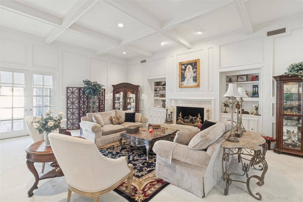 6215 Raintree Court, Dallas, TX 75254 Coffered ceiling, custom wall paneling, built-in shelving, fireplace with decorative surround, and multi-pane glass doors