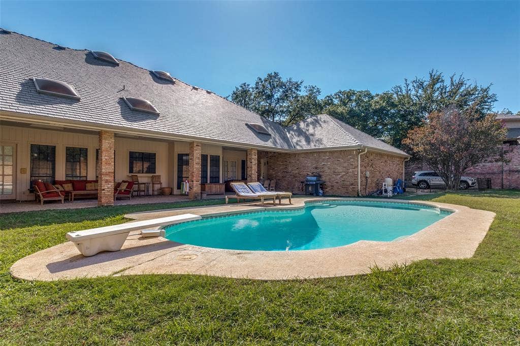 6215 Raintree Court, Dallas, TX 75254 Backyard featuring a swimming pool with a diving board, a covered patio with brick columns, and multiple roof-mounted skylights