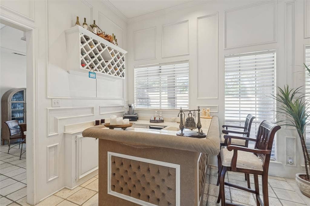 6215 Raintree Court, Dallas, TX 75254 Built-in wet bar featuring stone-finish countertop, grid-style bottle storage, and decorative wall molding