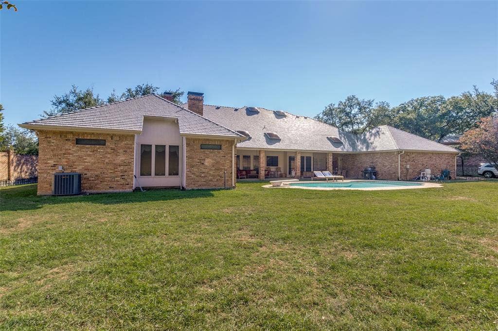 6215 Raintree Court, Dallas, TX 75254 Brick exterior residence featuring a sprawling lawn, a rear covered patio, an in-ground swimming pool, and roof-integrated skylights