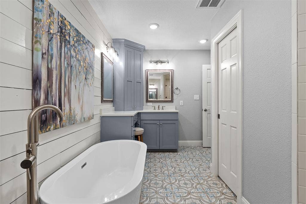 200 Oriental Road, Waco, TX 76710 Freestanding soaking tub with a floor-mounted brushed nickel faucet, custom blue cabinetry with integrated tower, patterned tile flooring, and shiplap wall detailing