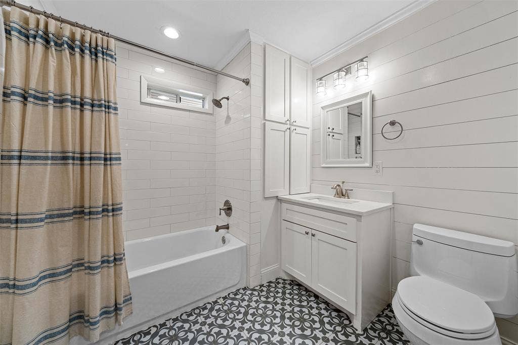 200 Oriental Road, Waco, TX 76710 Bathroom featuring horizontal shiplap walls, patterned tile flooring, white shaker-style vanity with a built-in linen cabinet, and white subway tile shower surround