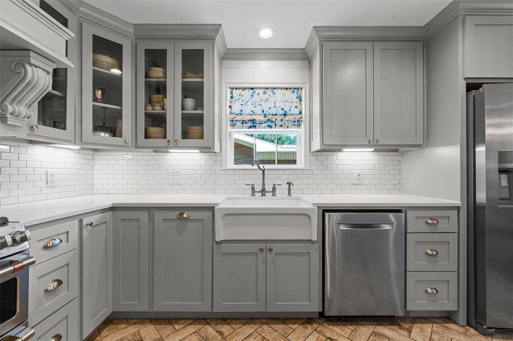 200 Oriental Road, Waco, TX 76710 Kitchen featuring gray shaker-style cabinetry with glass-front uppers, white subway tile backsplash, farmhouse-style apron sink, and herringbone-patterned flooring