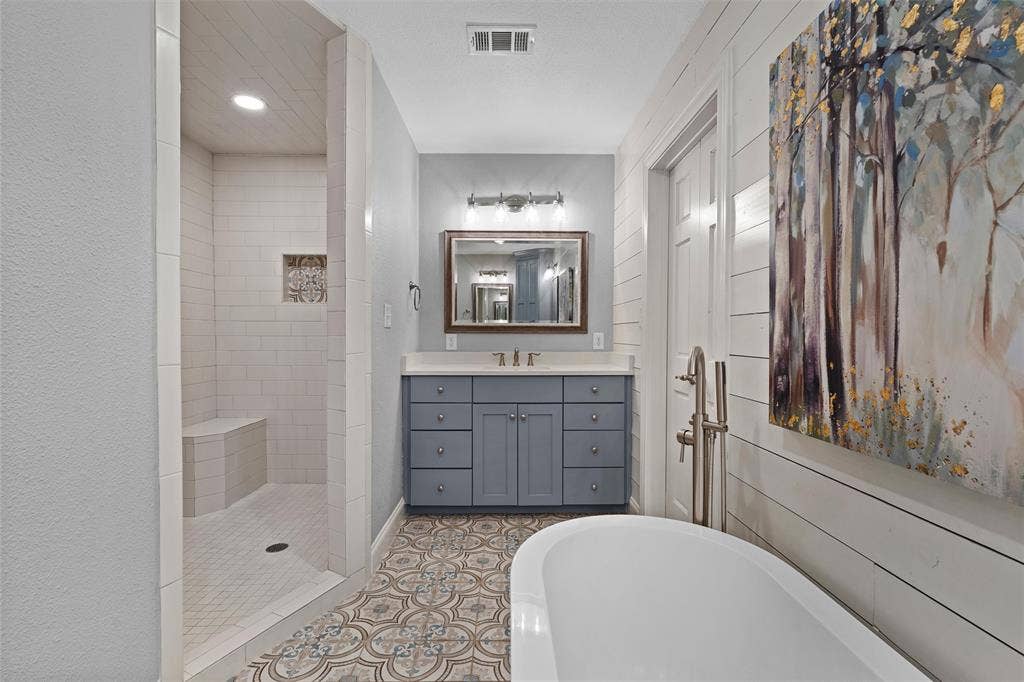 200 Oriental Road, Waco, TX 76710 Bathroom featuring a freestanding tub, walk-in shower with built-in seating, dual-tone vanity cabinet, patterned floor tile, and horizontal wall paneling