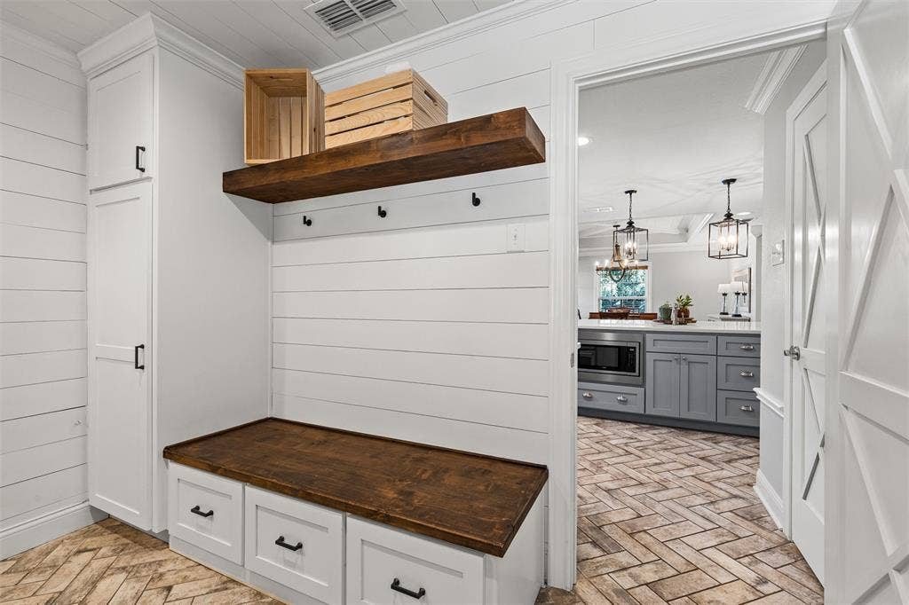 200 Oriental Road, Waco, TX 76710 Custom built-in mudroom bench with a wood-finish top and lower storage drawers, white shiplap wall paneling, stained wood floating shelf, tall floor-to-ceiling cabinetry, and herringbone-patterned flooring