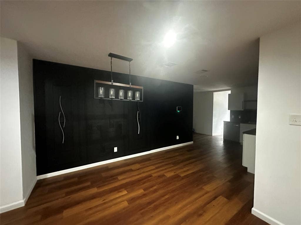 4808 Sandra Lynn Drive, Mesquite, TX 75150 Wood-finish flooring, accent wall with textured detailing, and a modern five-light rectangular chandelier