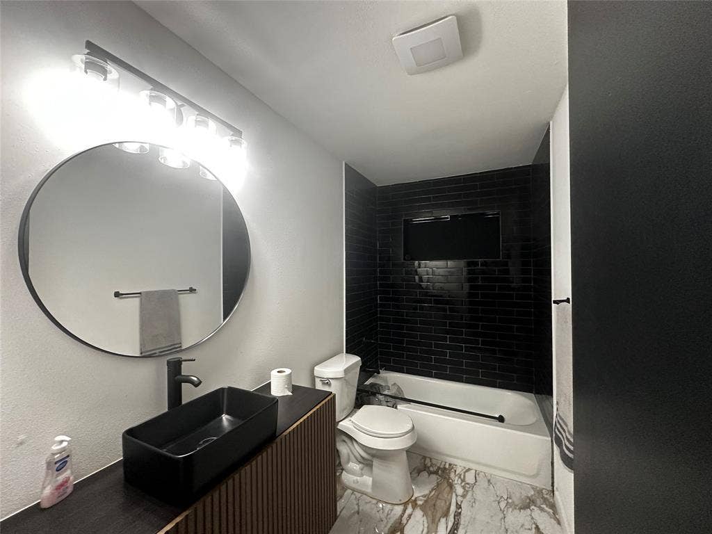 4808 Sandra Lynn Drive, Mesquite, TX 75150 Modern vanity with vertical slat detailing, rectangular vessel sink, matte black faucet, circular wall mirror, and tub enclosure with black subway tile surround
