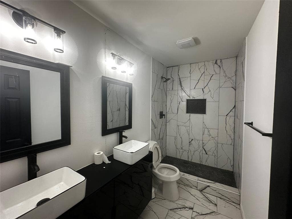 4808 Sandra Lynn Drive, Mesquite, TX 75150 Bathroom featuring a dual vanity with white vessel sinks, black matte hardware, framed mirrors, and a walk-in shower with veined tile surround and built-in niche