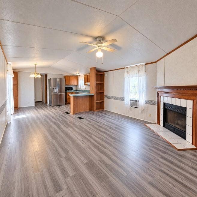 Wood-finish flooring, fireplace with a tile surround and wood mantel, built-in shelving, wood cabinetry, and a ceiling fan